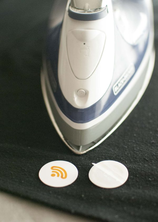 Two iron-on NFC tags next to an iron on a piece of black fabric